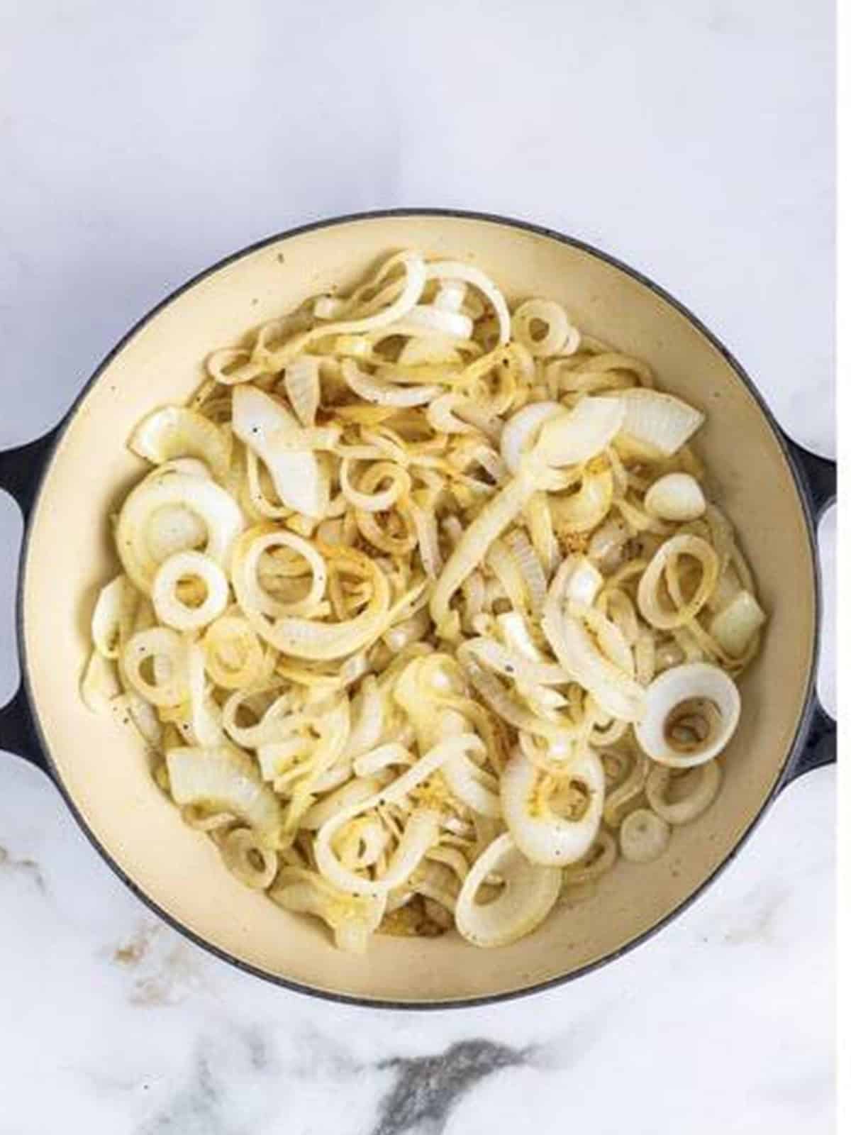 Sweet onion rings cooking in olive oil in a large skillet for Caramelized Onions.