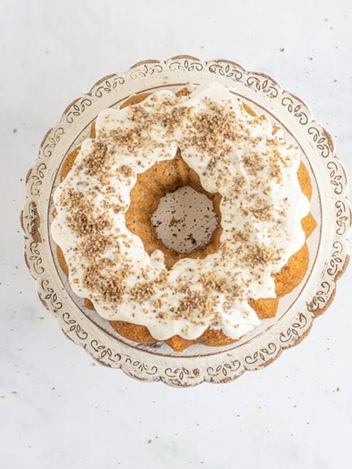 Carrot bundt cake drizzled with cream cheese glaze and topped with chopped pecans.