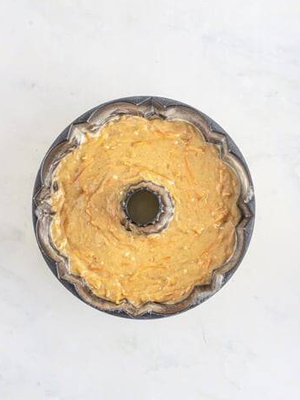 Carrot cake batter spread into a greased bundt pan.