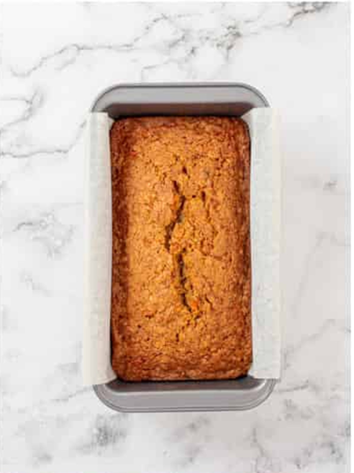 Golden baked carrot loaf cake in the pan with a cracked top.