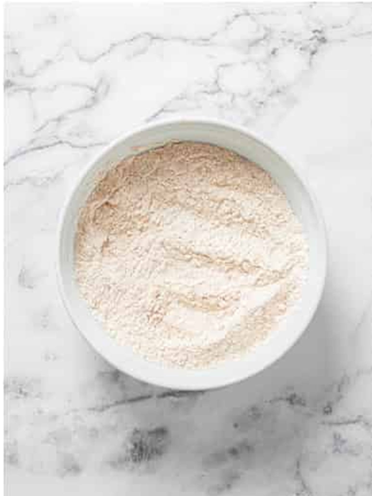 Flour, baking soda, and warm spices combined in a white bowl for carrot loaf cake.