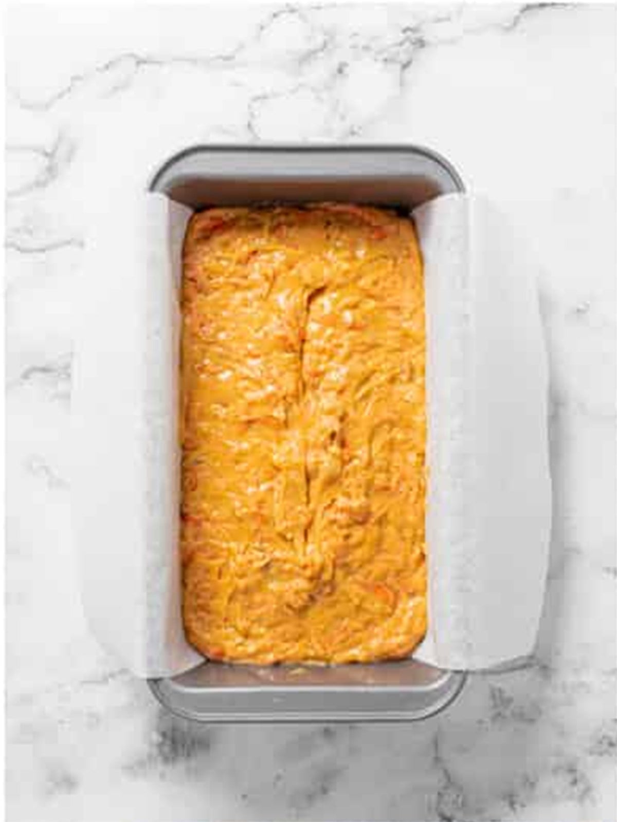 Carrot loaf cake batter spread into a parchment lined loaf pan.