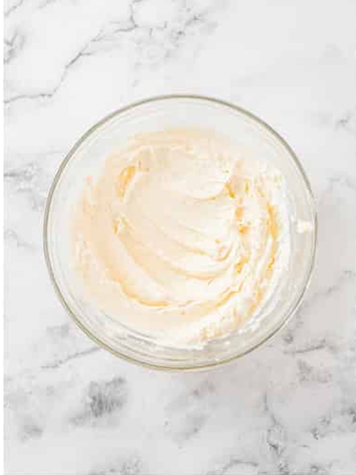 Cream cheese frosting whipped smooth in a glass bowl.