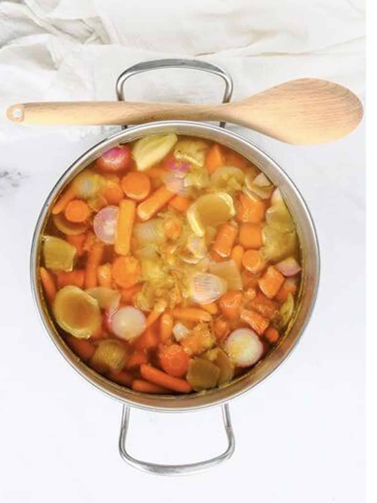 Sliced carrots, onion, radishes, and garlic cooking in vegetable broth in a pot.