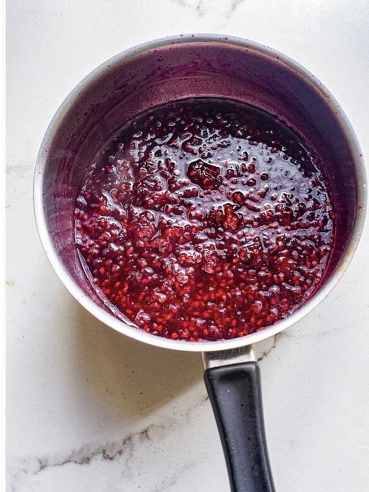 Blackberries simmering and breaking down in a saucepan.
