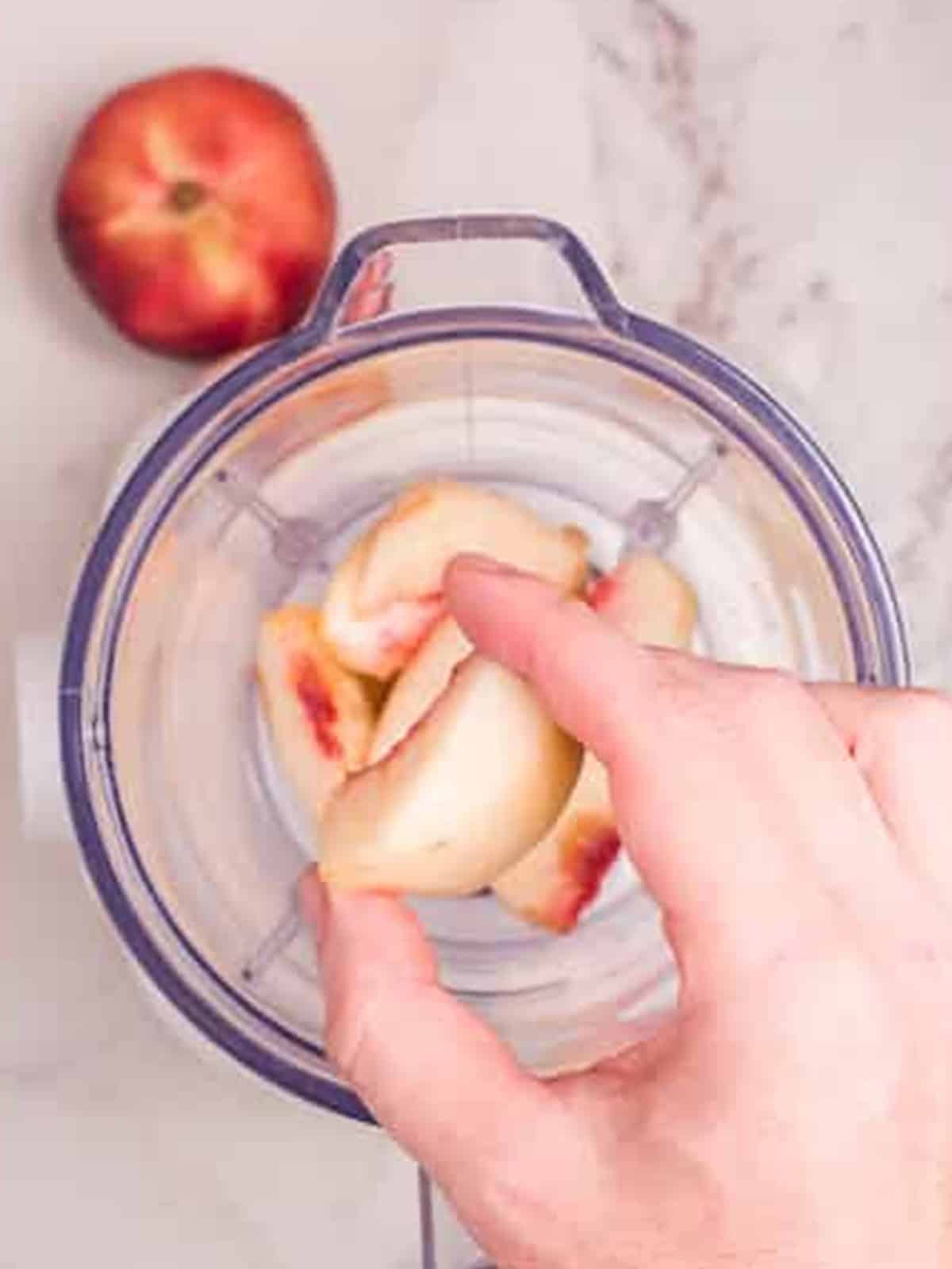 Adding fresh peach slices to a blender.
