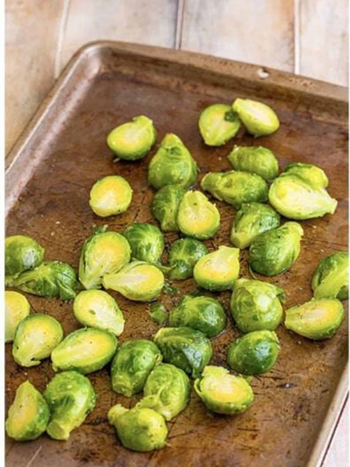 Brussels sprouts tossed with bacon fat on a baking sheet.