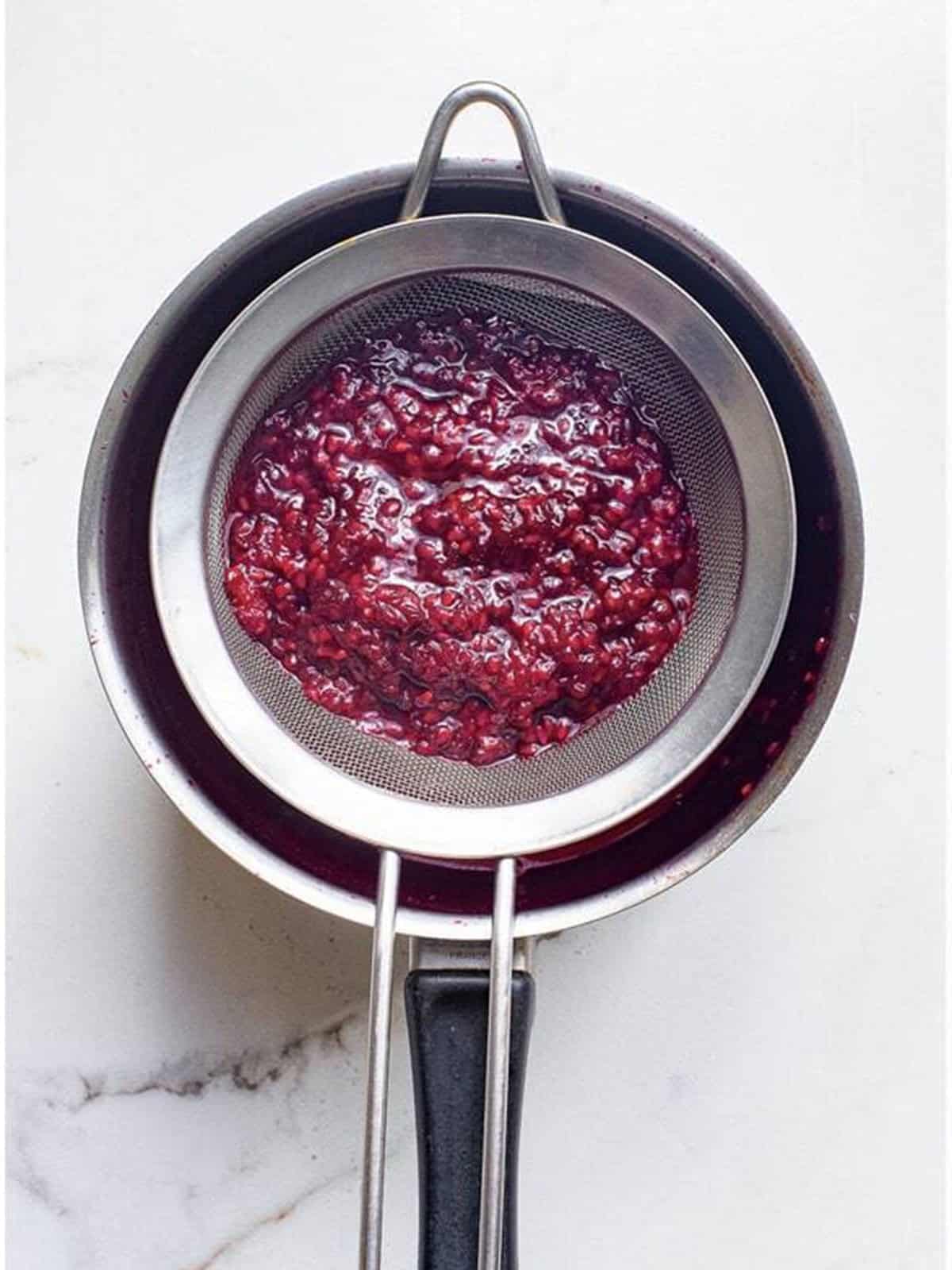 Straining the blackberry sauce through a fine mesh sieve.
