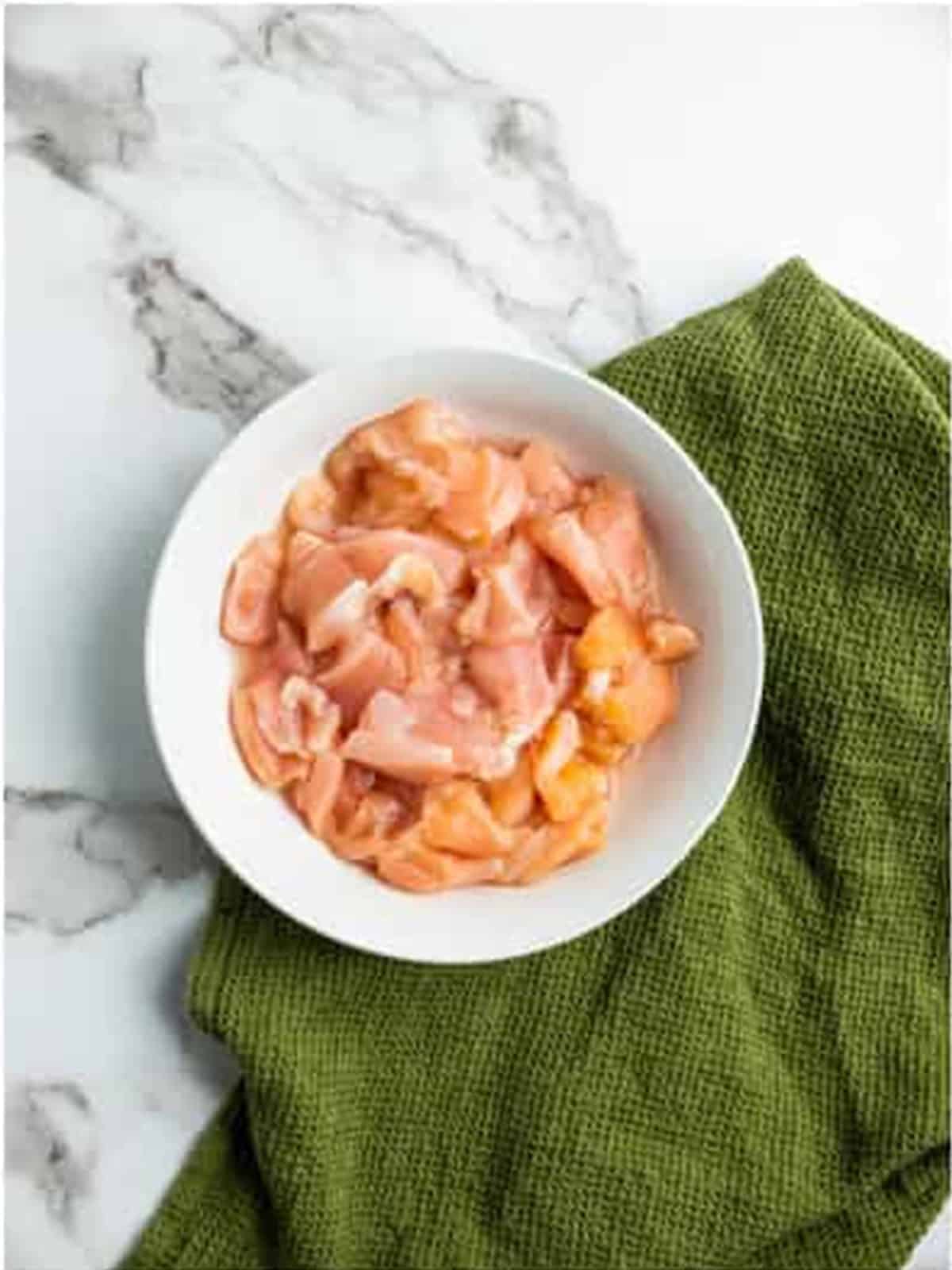 Sliced raw chicken breast in a white bowl for drunken noodles.