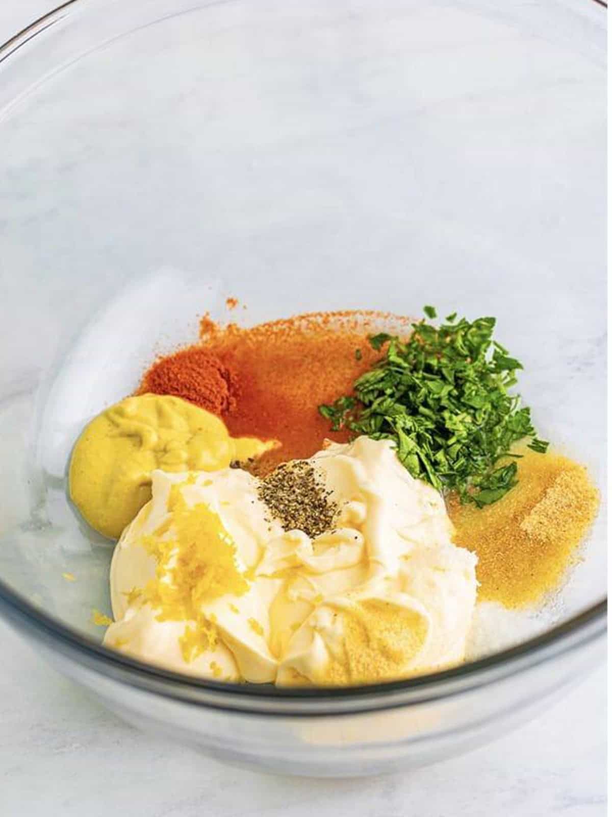 Mayonnaise, dijon mustard, lemon, and seasonings in a glass bowl to make chicken salad dressing.
