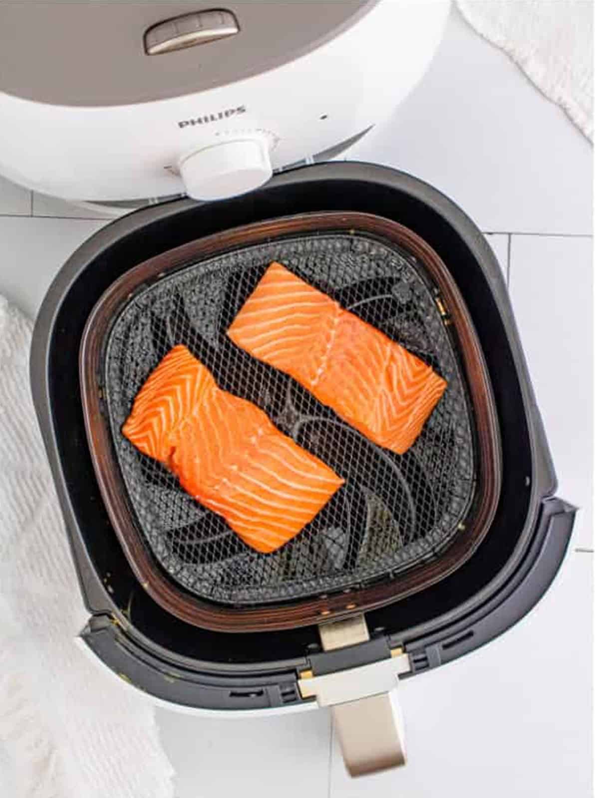 Raw salmon filets placed skin side down in the air fryer basket.