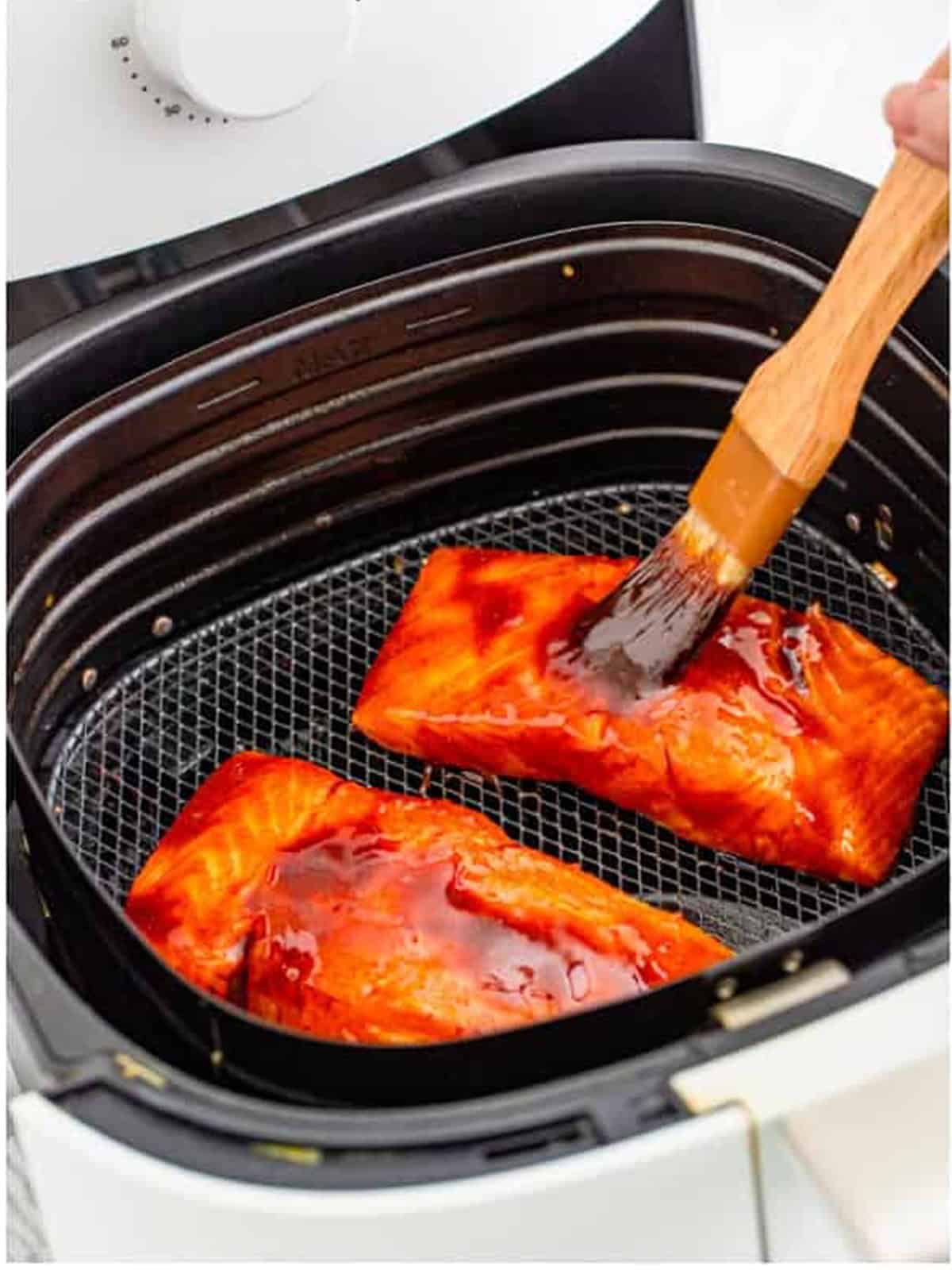 Brushing the Asian glaze over salmon filets in the air fryer basket.