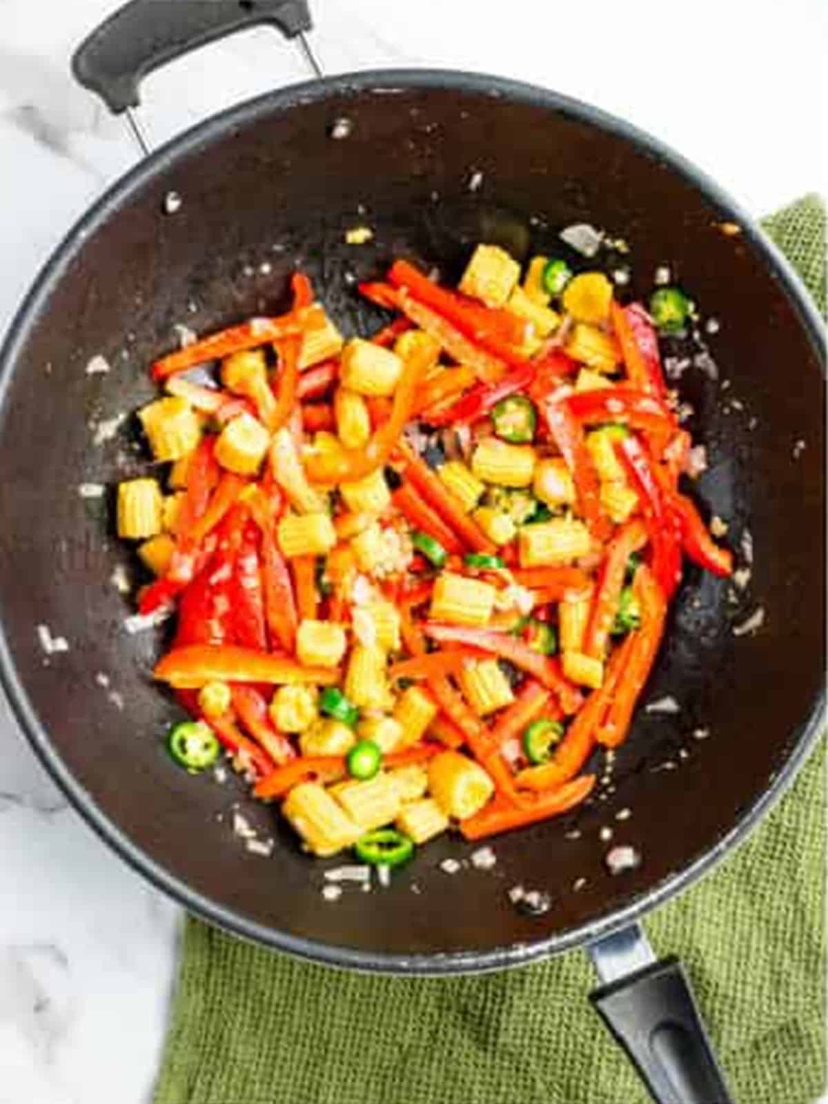 Adding red bell peppers, chilies, and baby corn to the wok.