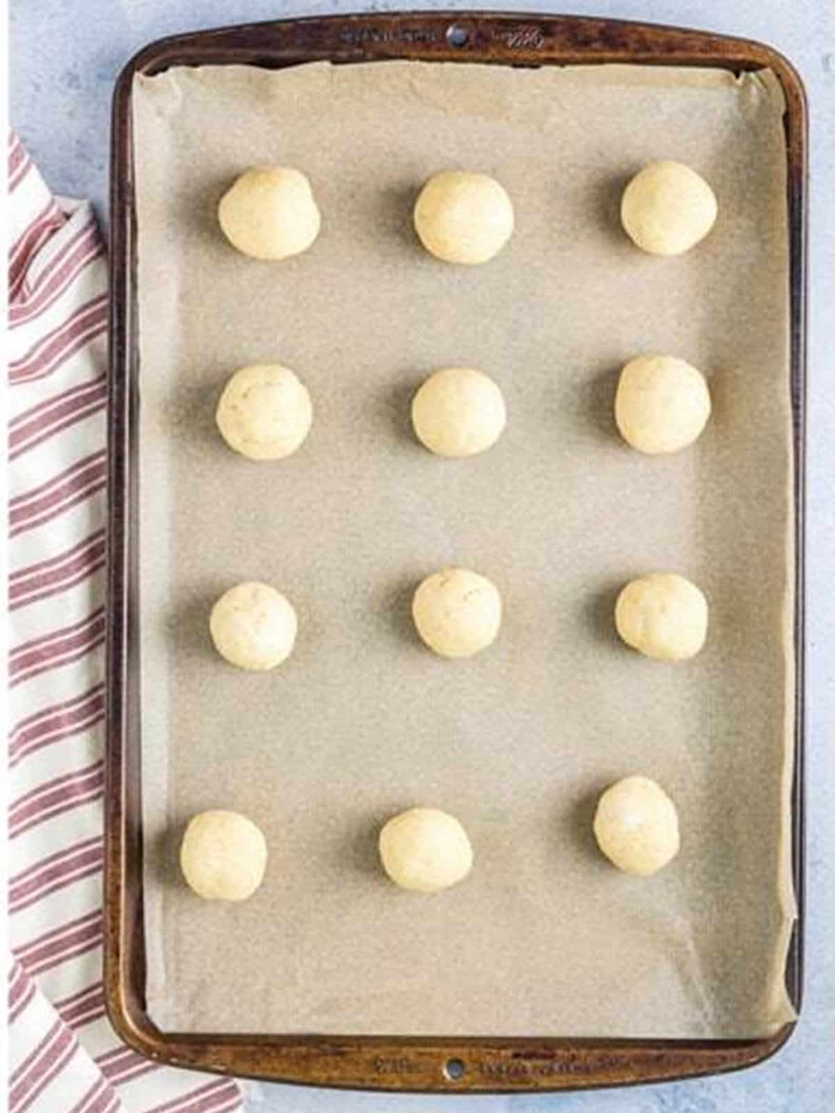 Rolled tea cake dough balls on a parchment lined baking sheet.