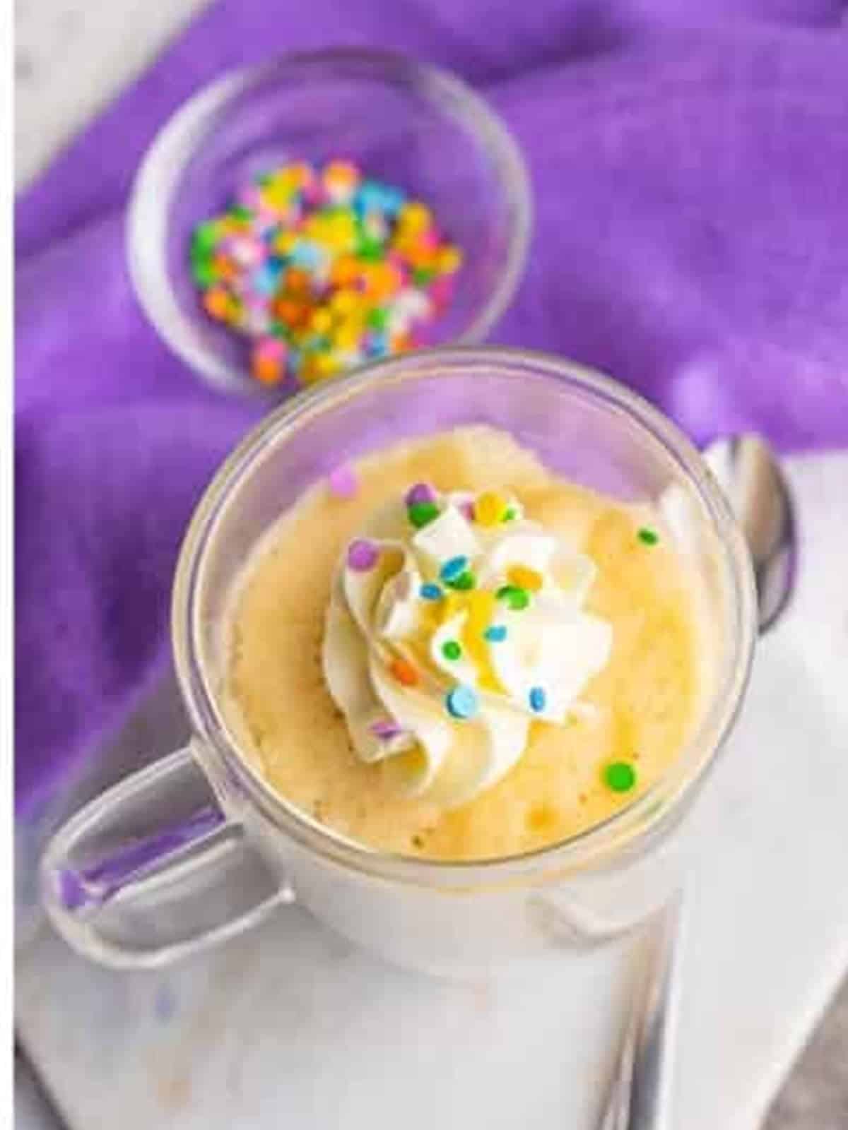 Finished vanilla mug cake topped with whipped frosting and sprinkles.