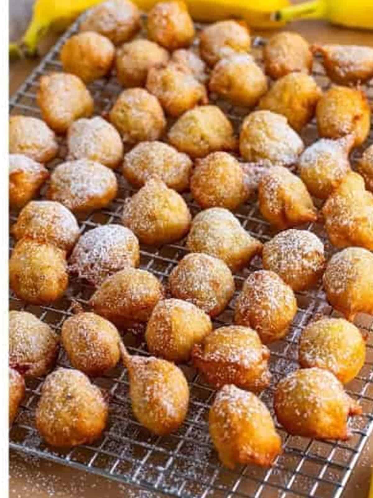 Banana fritters dusted with powdered sugar on a wire rack.