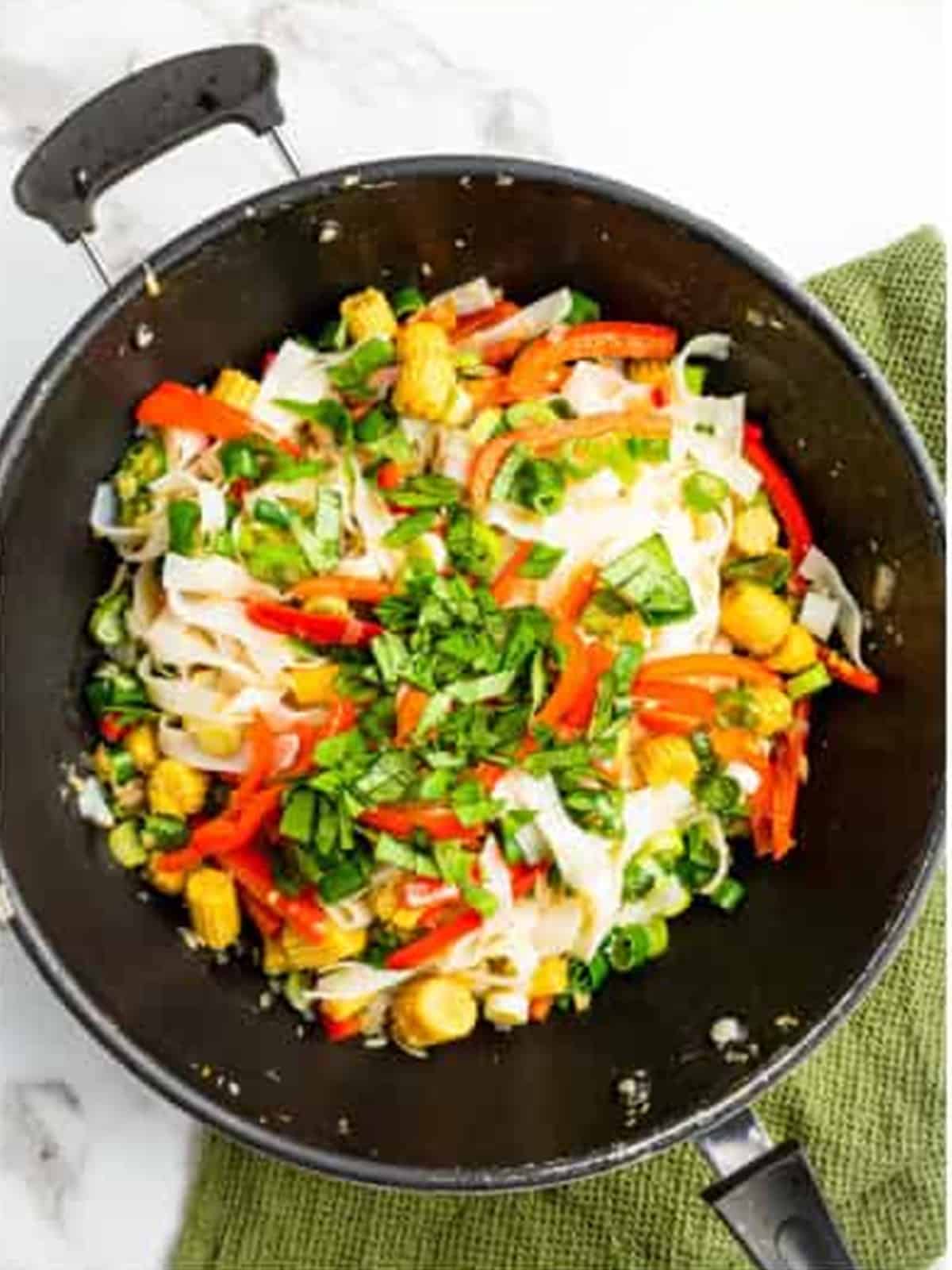 Adding cooked rice noodles, Thai basil, and chicken to the wok.