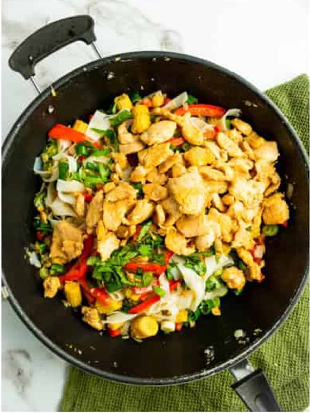 Tossing the drunken noodles with the sauce using tongs.