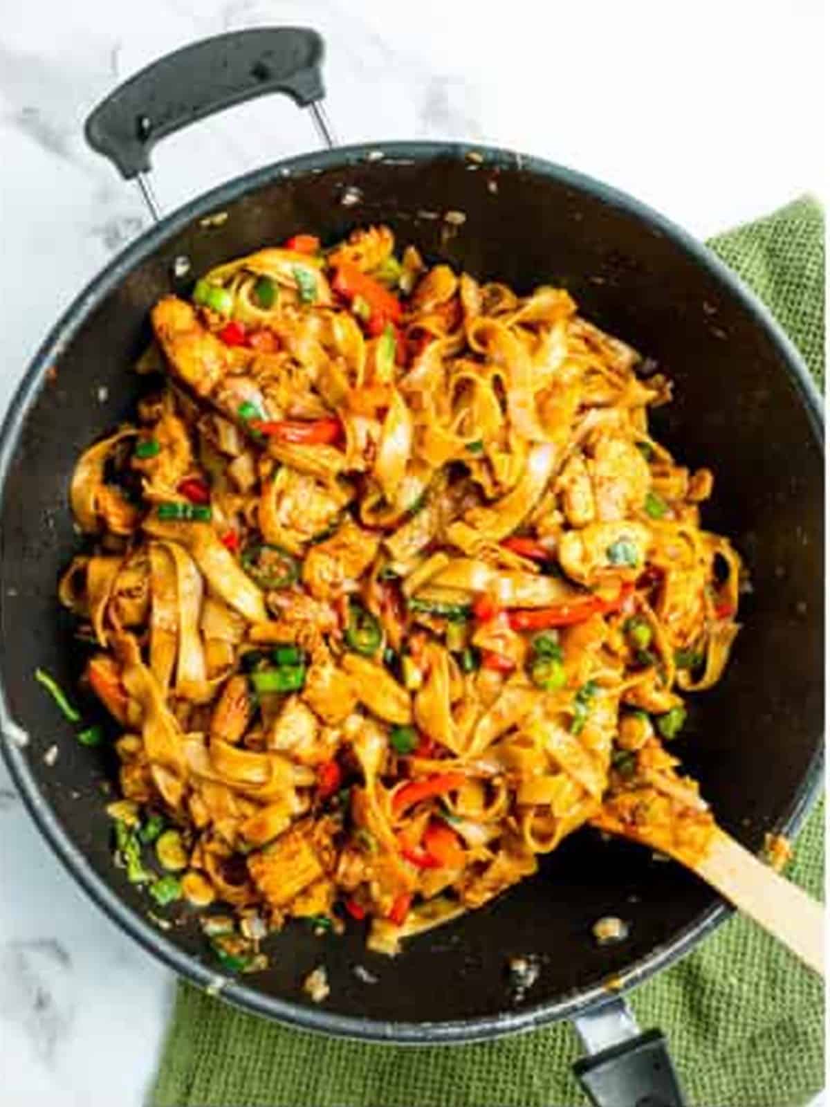 Finished Thai drunken noodles in the wok garnished with Thai basil.