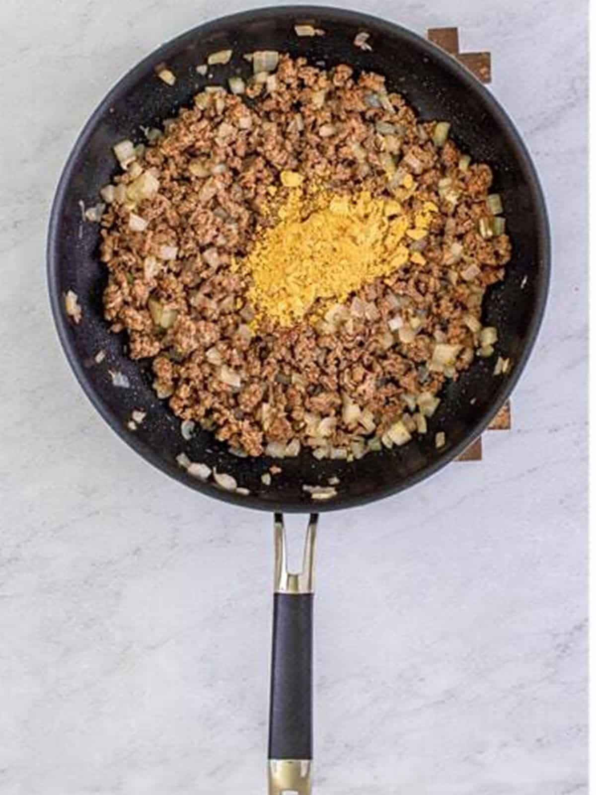 Ground beef and onion browning in a skillet with taco seasoning.