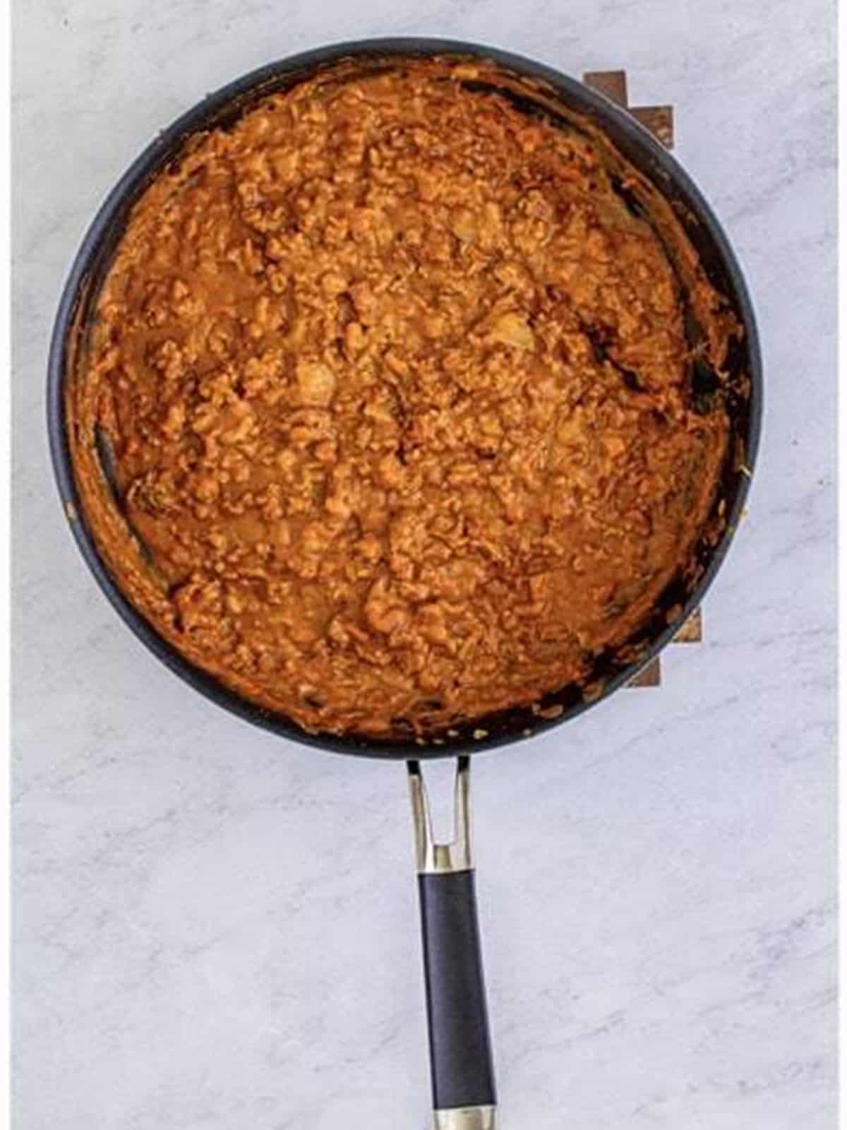 Refried beans mixed into the seasoned beef filling in a skillet.