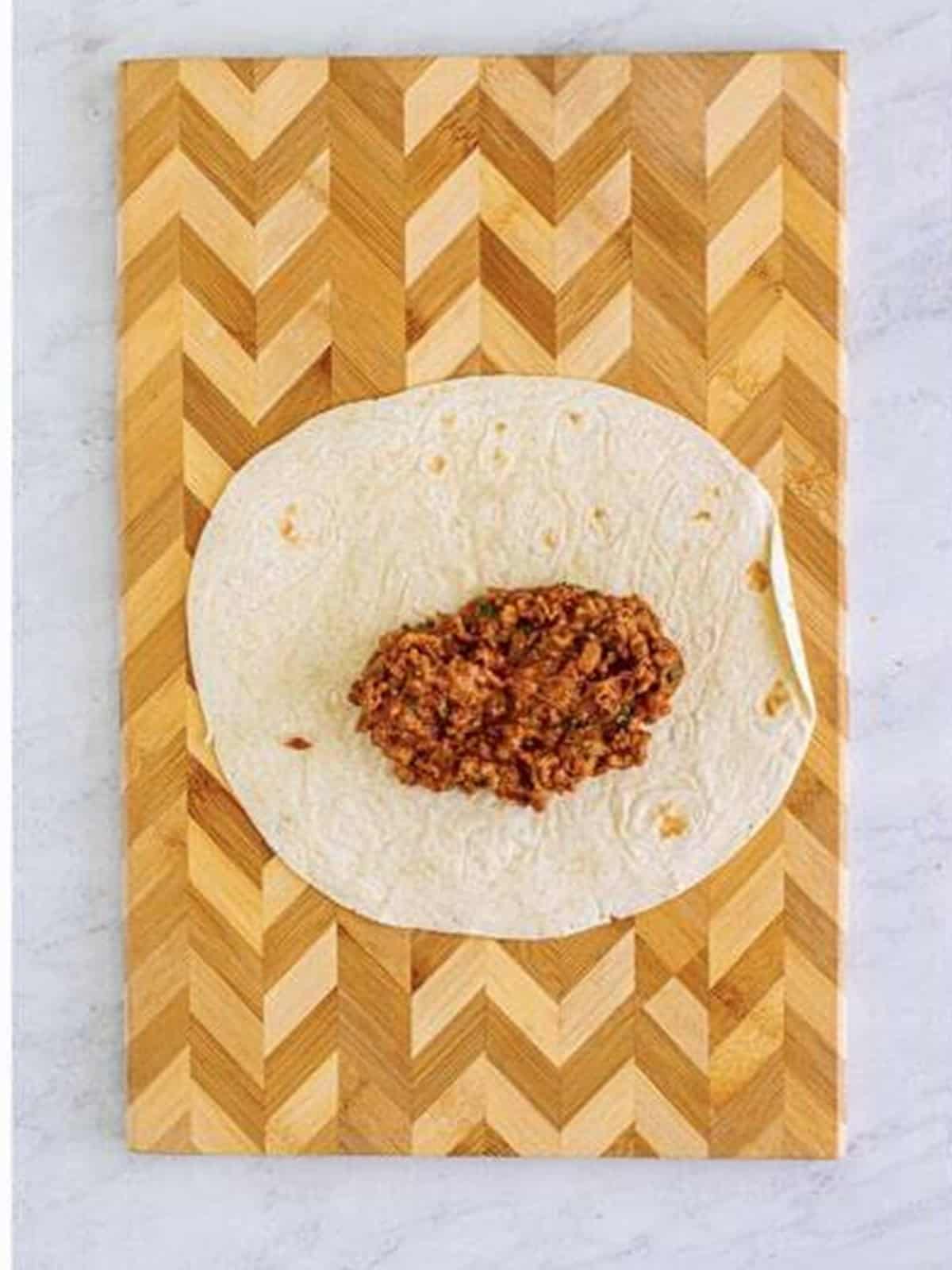 Beef filling and cheese spooned onto a flour tortilla for smothered burritos.
