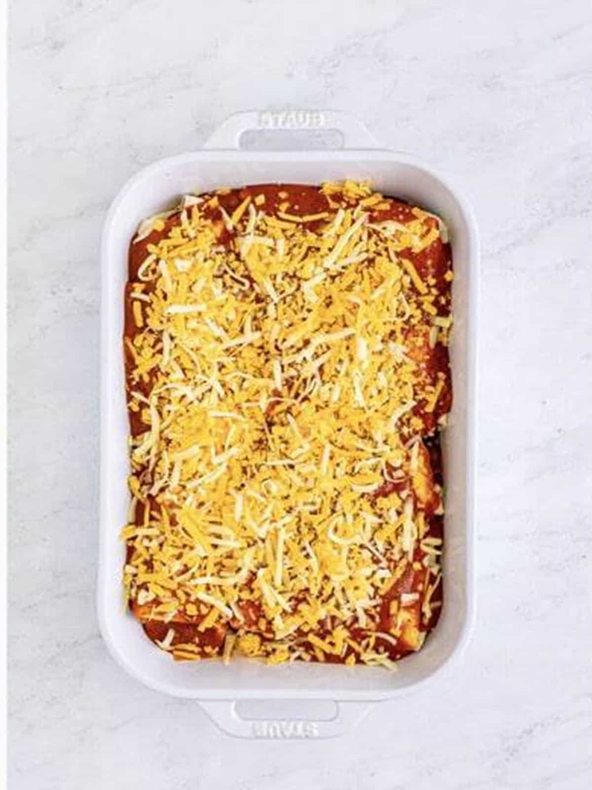 Rolled burritos topped with red sauce and shredded cheese in a baking dish.