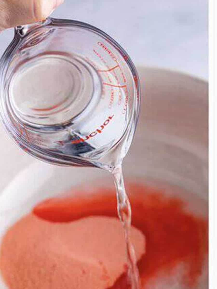 Pouring boiling water into strawberry banana jello mix in a bowl.