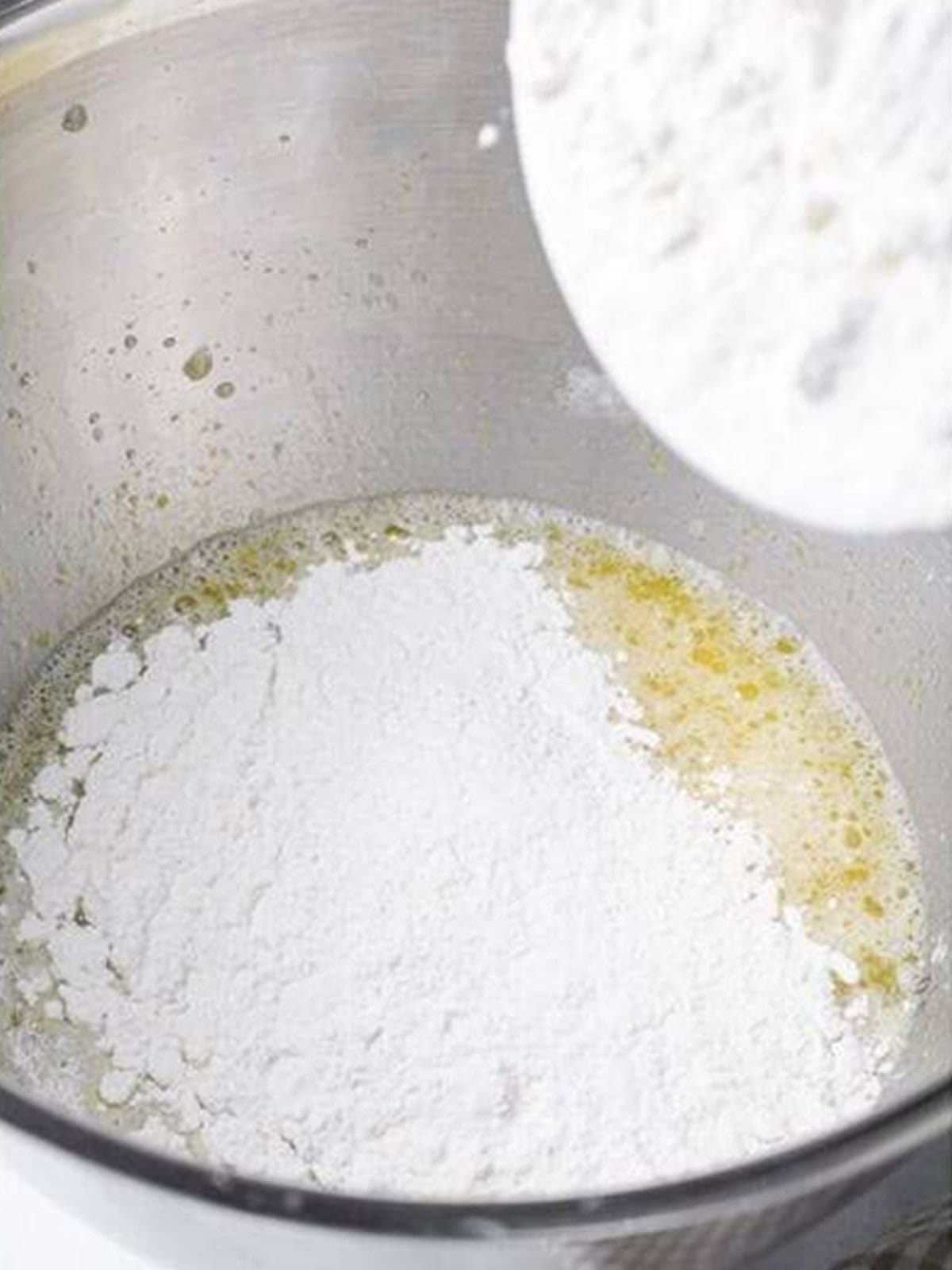 Flour being added to the wet ingredients in a mixer bowl to make challah bread dough.