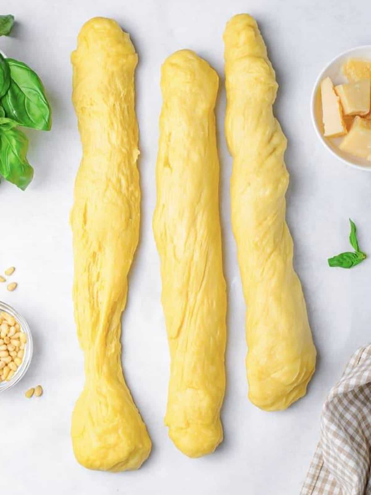Challah bread dough divided into three long ropes on parchment paper.
