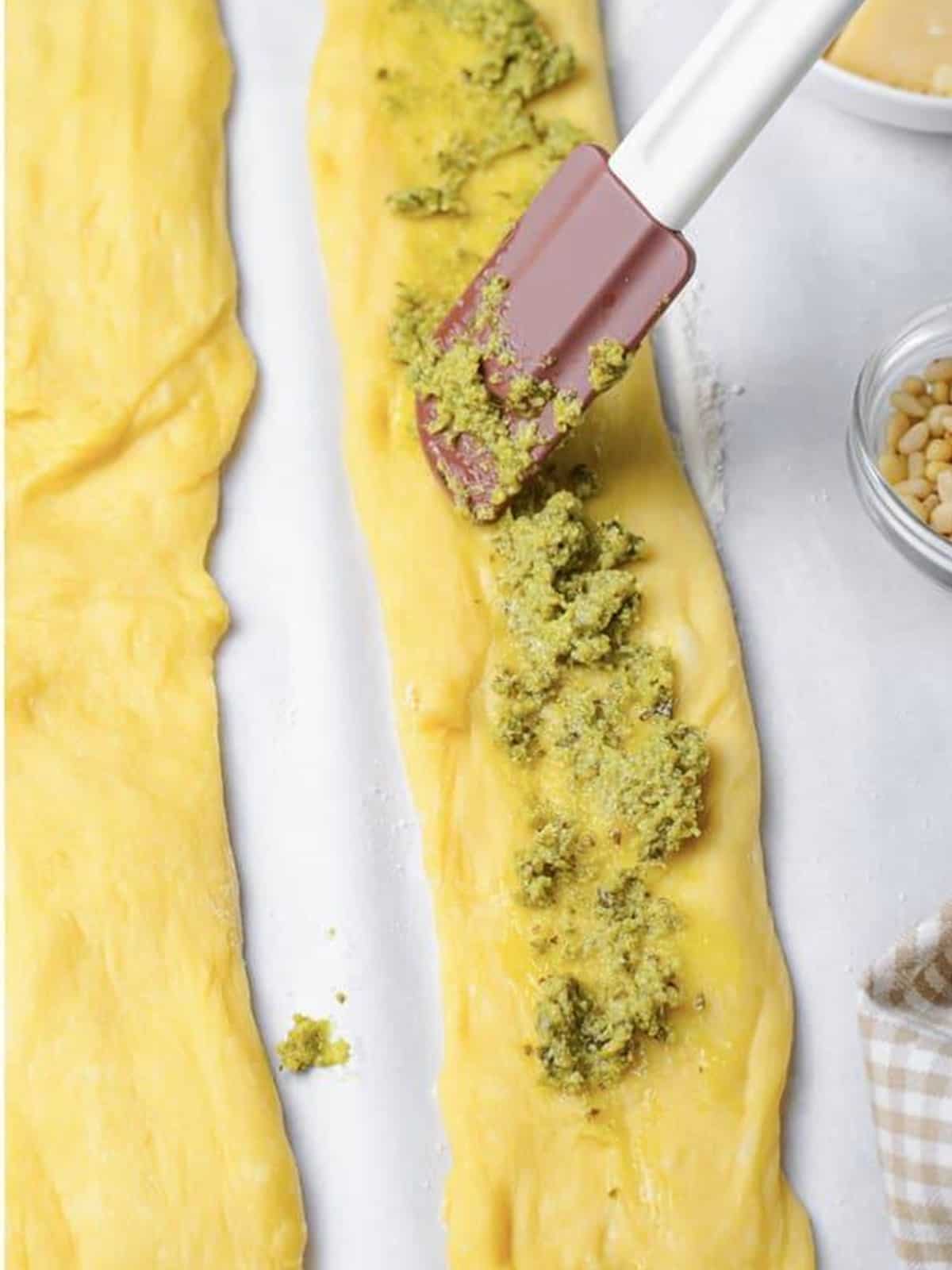 Pesto being spread down the center of a flattened challah bread dough rope.