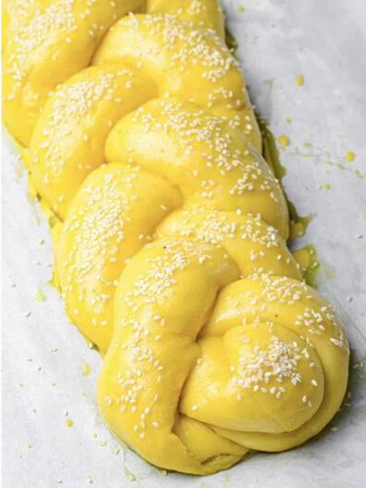 Braided challah bread brushed with egg wash and sprinkled with sesame seeds before baking.