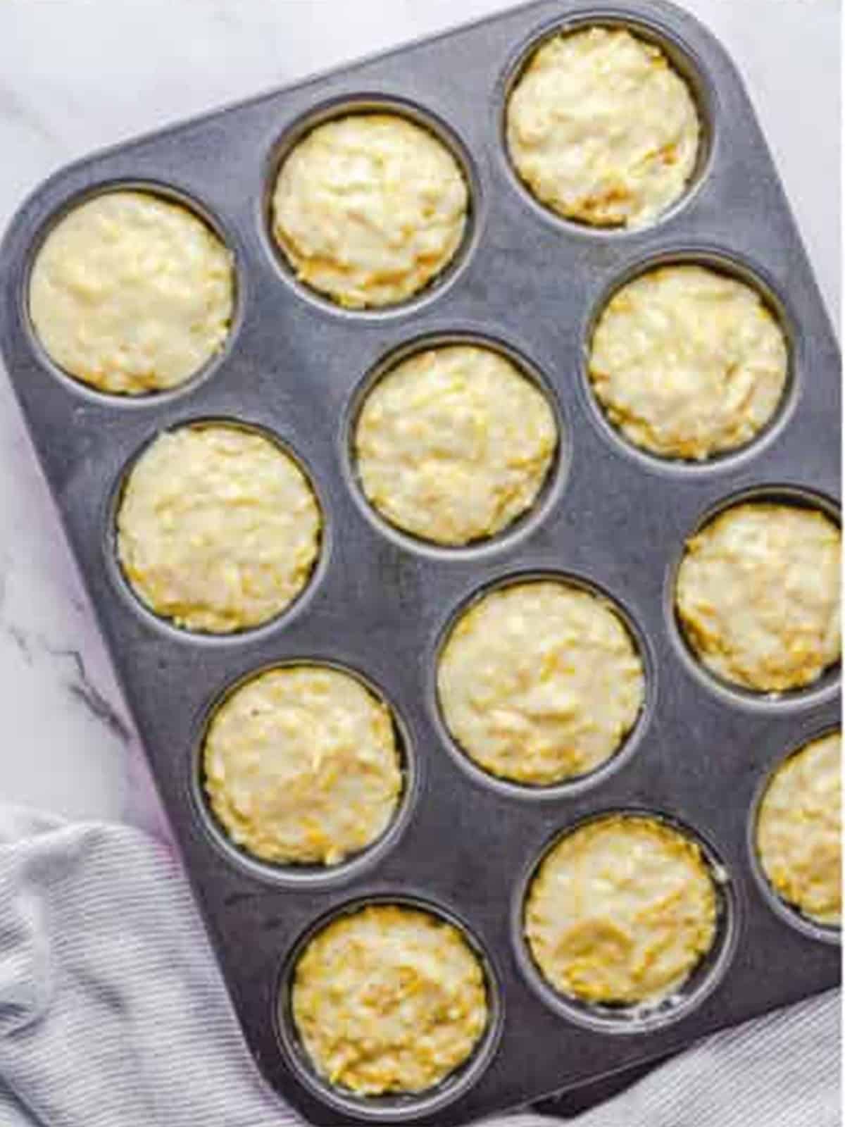 Cheese muffin batter divided evenly between the sections of a muffin tin.