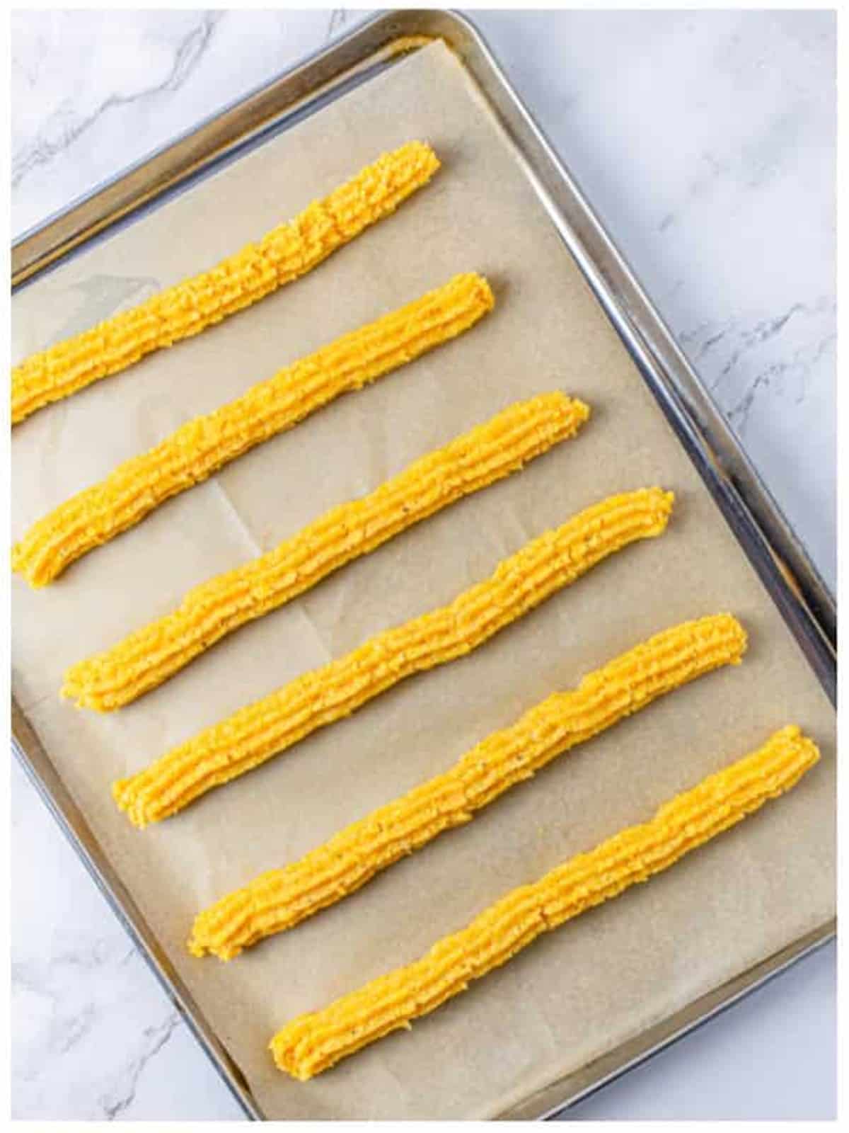 Cheese straw dough piped into long straws on a baking tray.