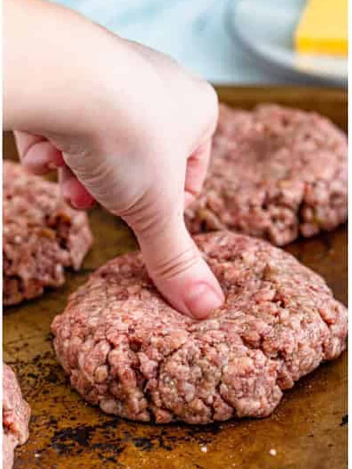 A hand forming seasoned ground beef into a cheeseburger patty.