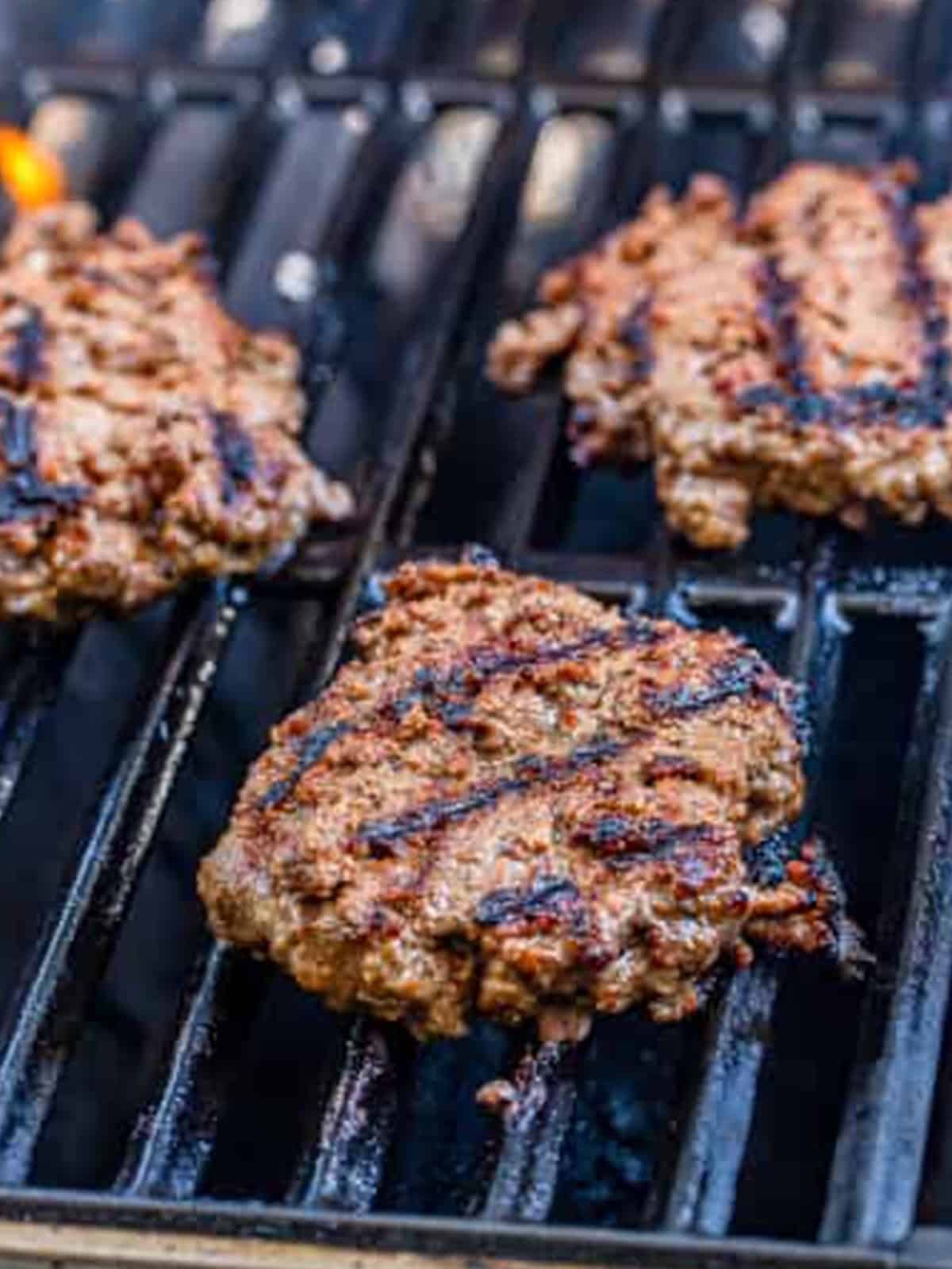 Cheeseburger patties grilling over high heat on grill grates.