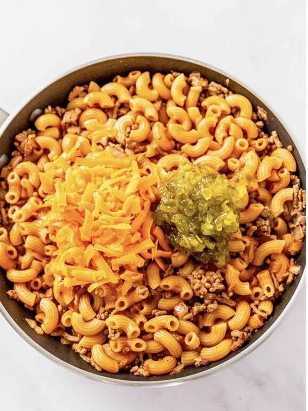 Stirring shredded cheddar and pickle relish into the Cheeseburger Pasta.