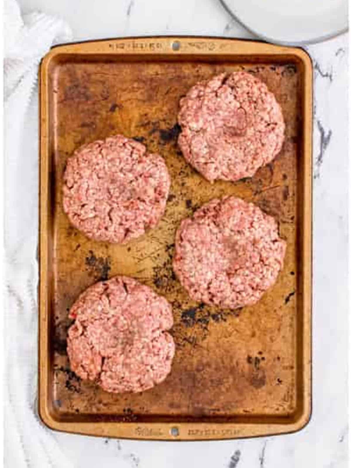 Four formed cheeseburger patties on a tray ready for the grill.