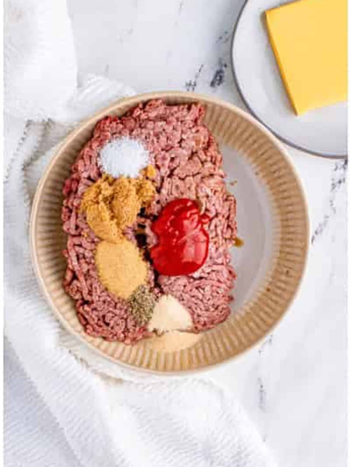 Ground beef with ketchup, Worcestershire, brown sugar, and seasonings in a bowl for cheeseburgers.