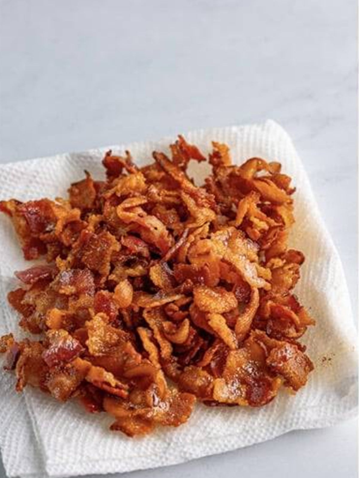 Crispy cooked bacon draining on a paper towel for cheeseburger soup.