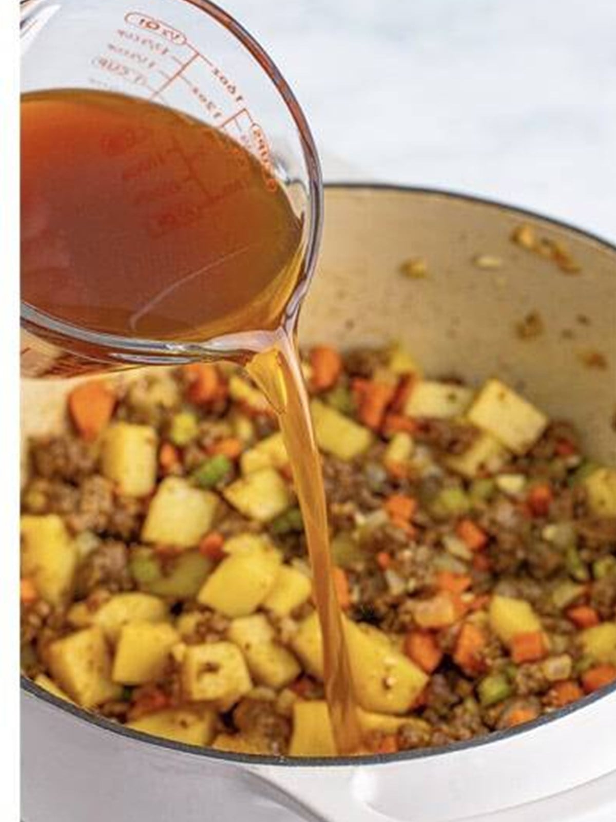 Beef stock being poured into the pot of ground beef and vegetables.