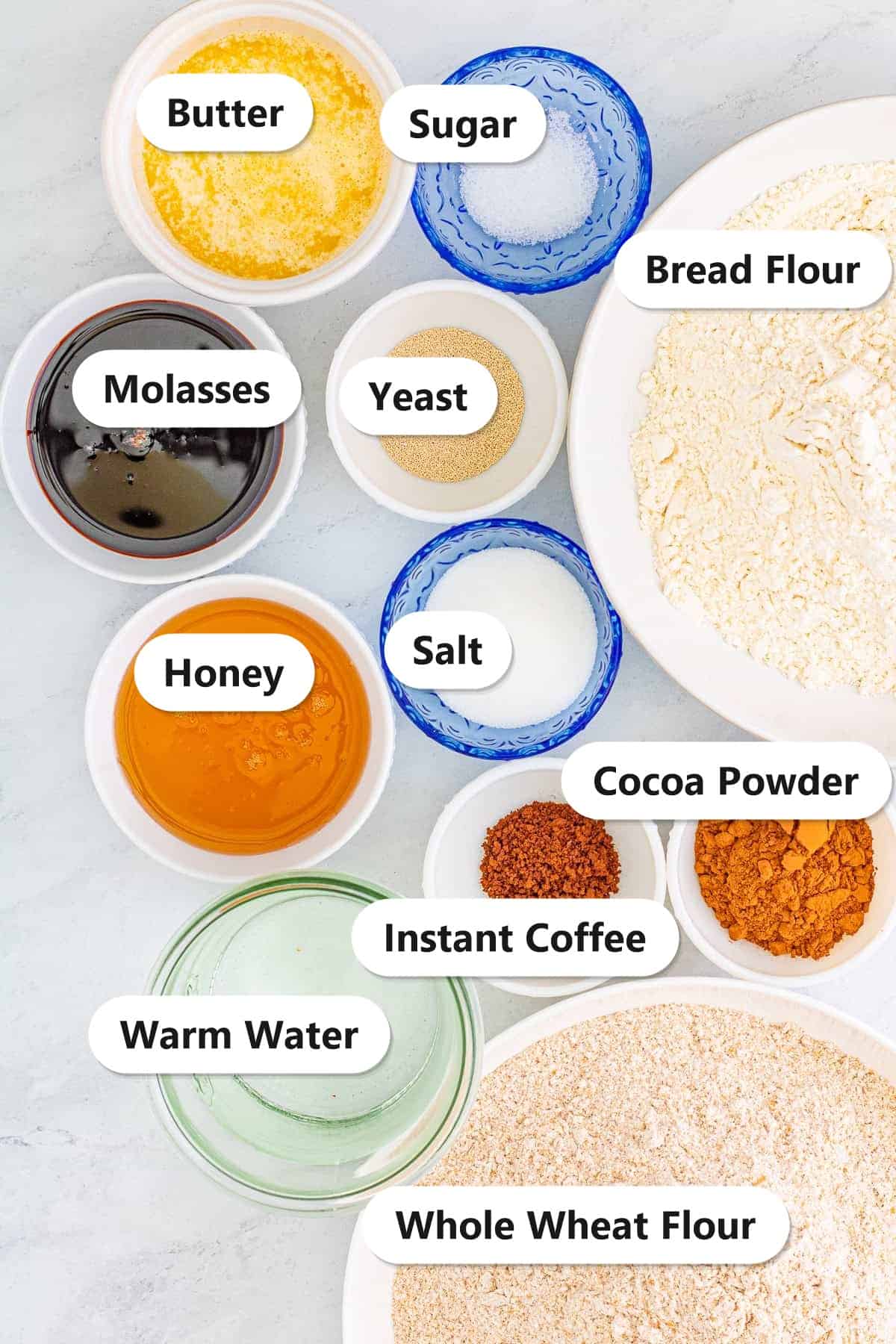 Labeled ingredients to make Cheesecake Factory brown bread including whole wheat flour, bread flour, cocoa powder, instant coffee, honey, molasses, butter, yeast, sugar, salt, and warm water.