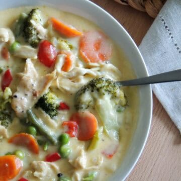 A bowl of creamy cheesy chicken and vegetable soup with broccoli, carrots, and peppers.