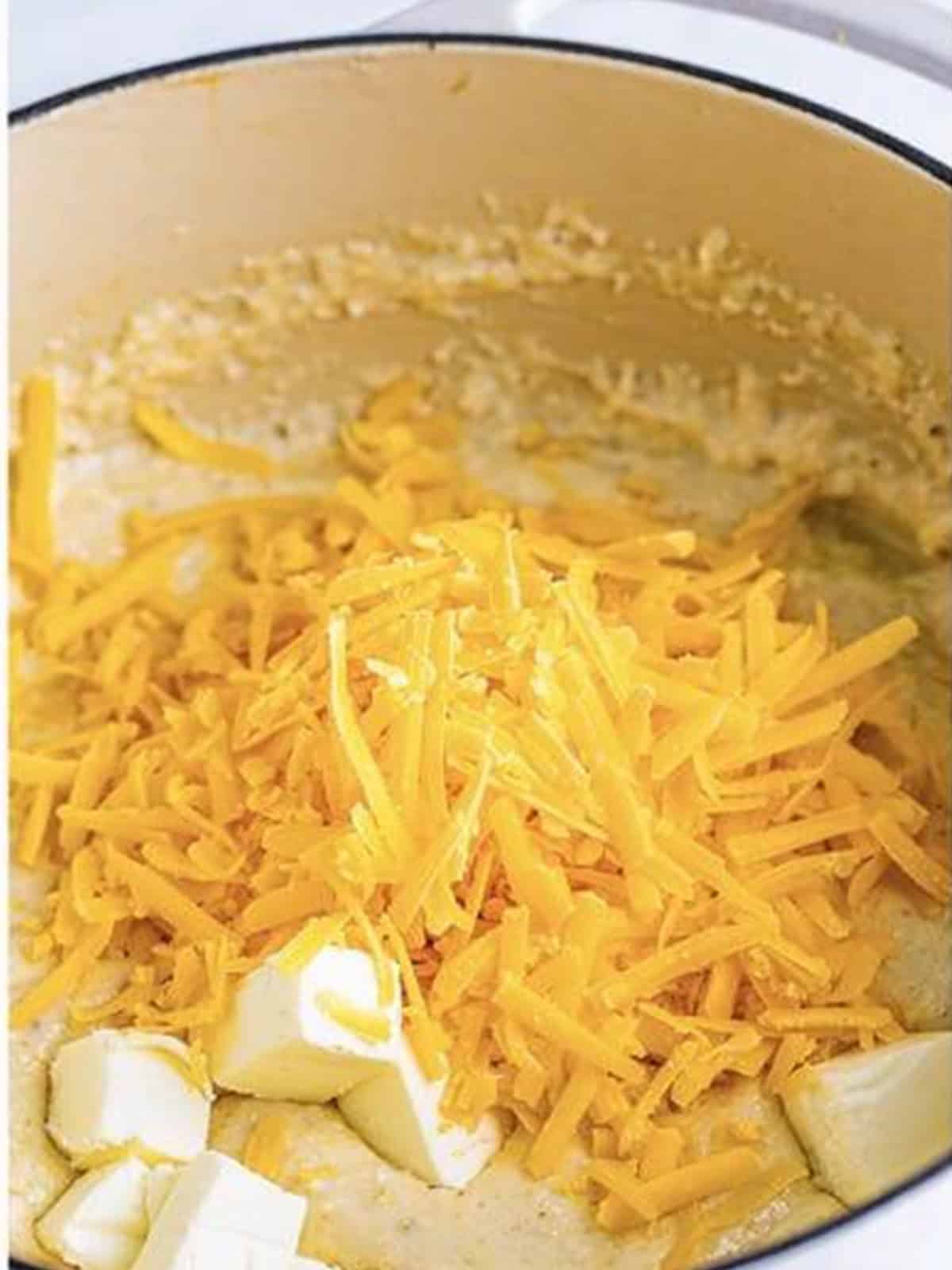 Cream cheese and shredded cheddar added to the creamy grits in the pot.