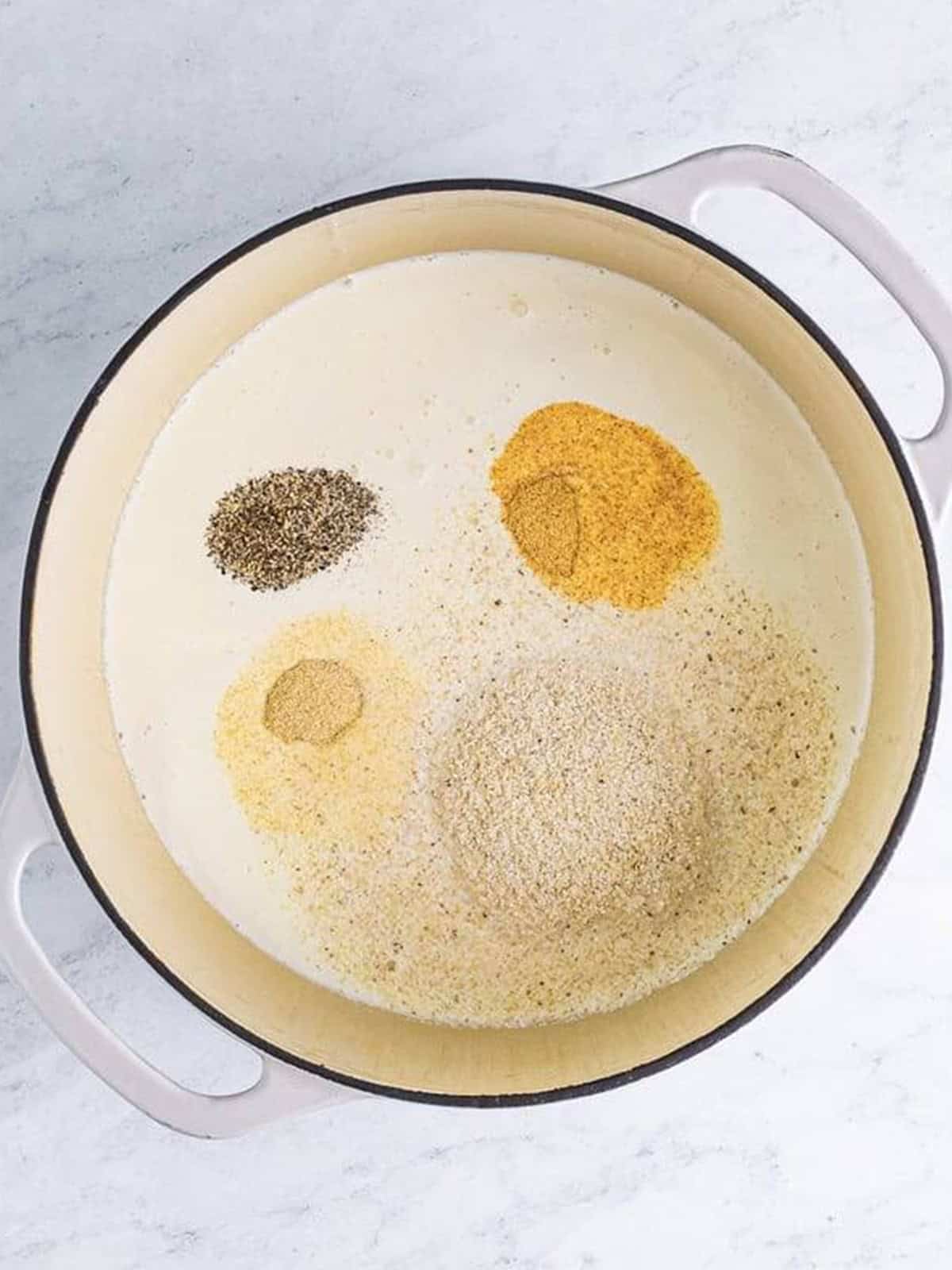 Heavy cream, chicken stock, grits, and spices combined in a pot to make cheesy grits.