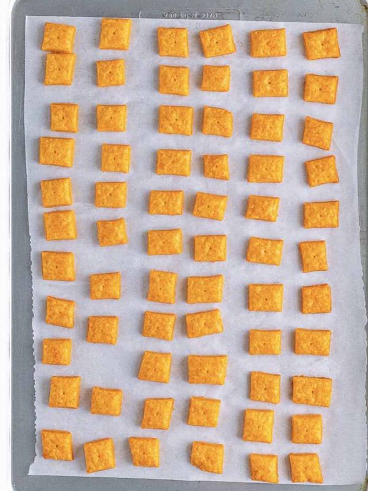Golden baked homemade Cheez-It crackers on a parchment-lined baking sheet.