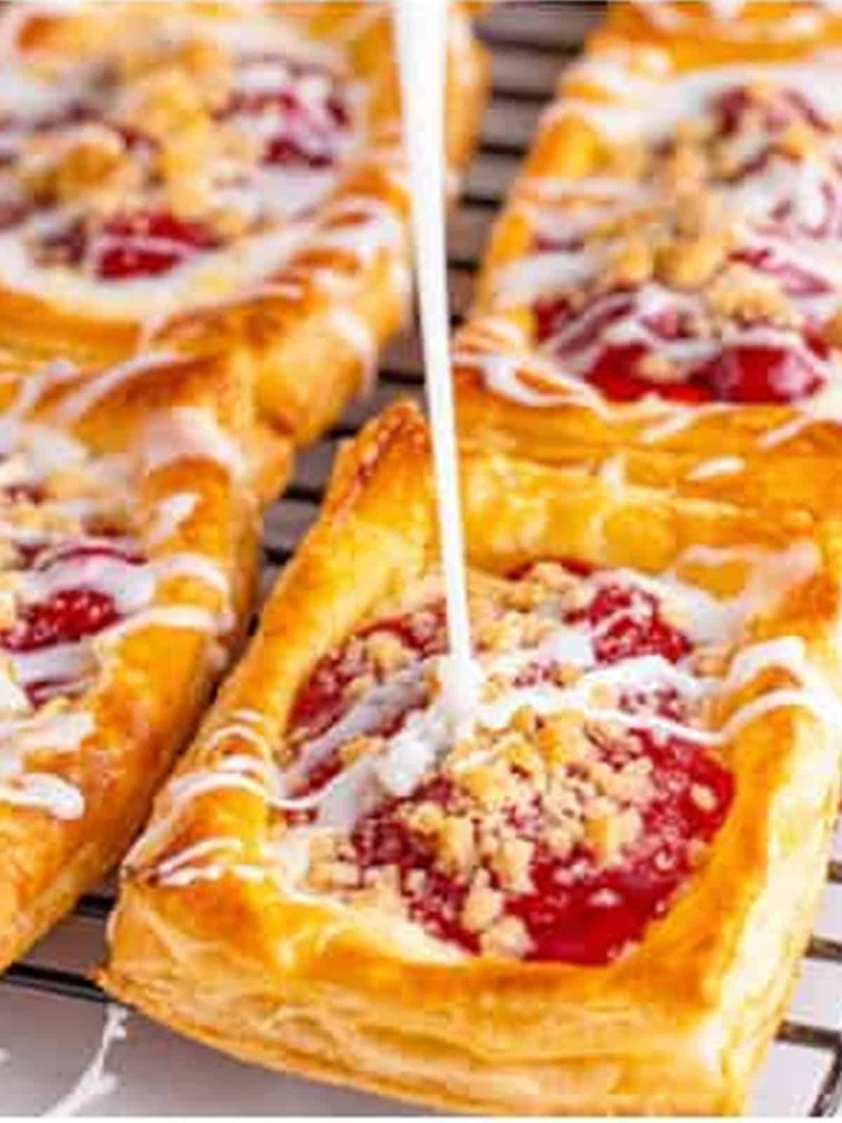 Vanilla glaze drizzled over baked Cherry Danishes on a wire rack.