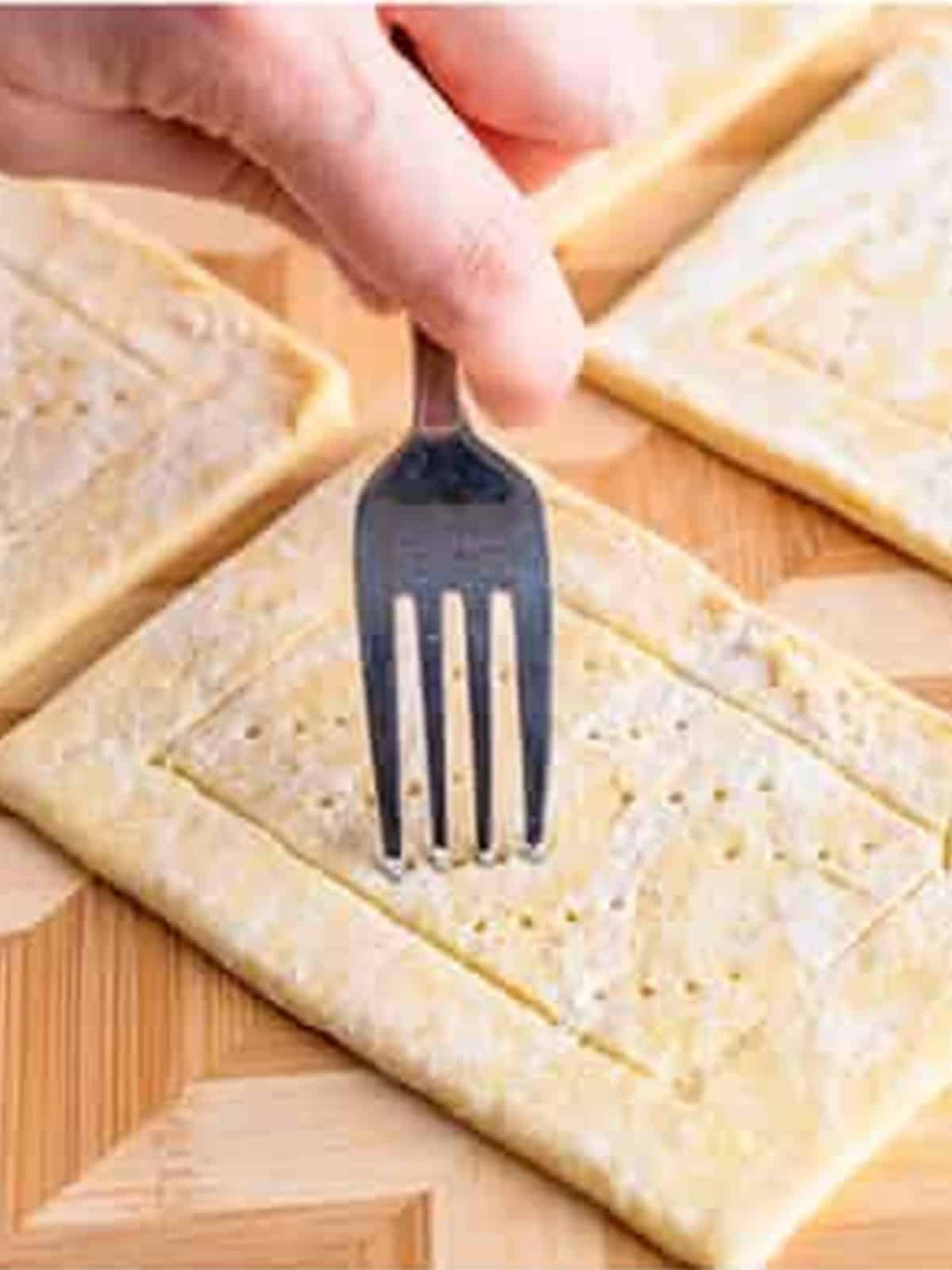 A fork poking holes in the center of a puff pastry rectangle for Cherry Danish.