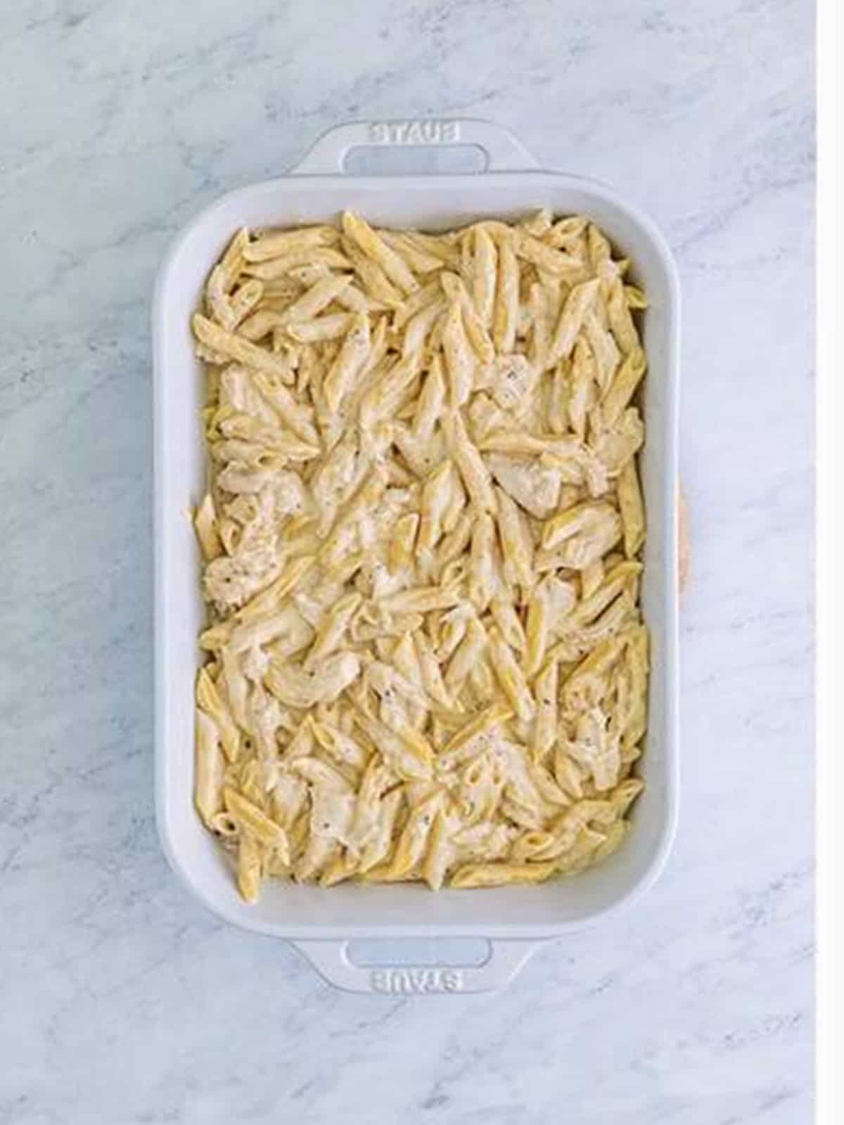 Chicken alfredo pasta layered in a white baking dish.