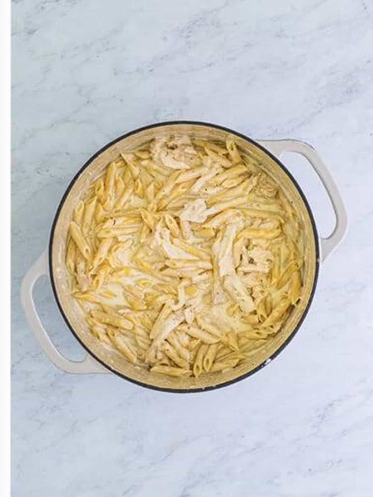 Penne pasta and shredded chicken coated in alfredo sauce in a pot.